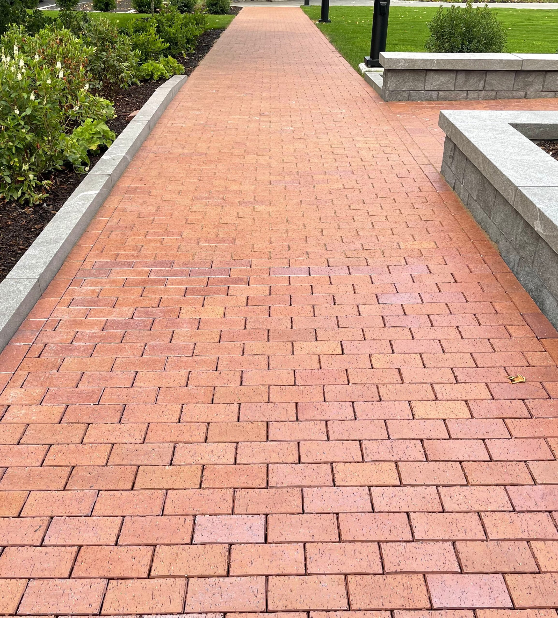 Paved walkway featuring interlocking concrete bricks, bordered by greenery and landscaping, highlighting Strathmeyer Landscape's installation services.