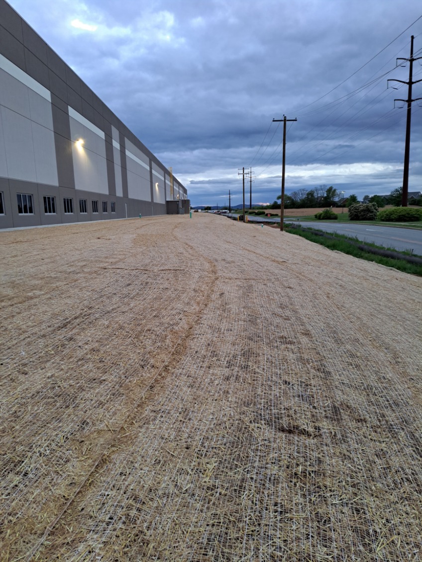 Landscaped area with straw matting for erosion control beside a commercial building, under a cloudy sky, highlighting Strathmeyer Landscape's installation services.