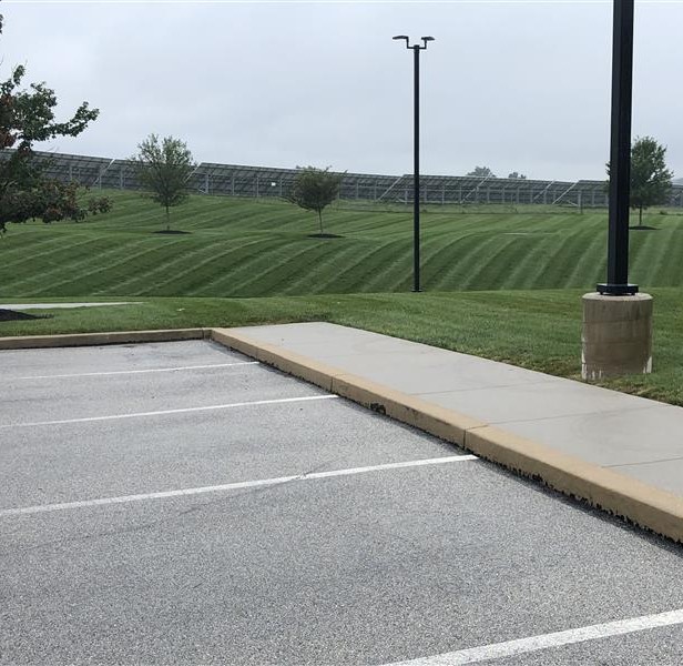 Landscaped area with neatly mowed grass, solar panels in the background, and a parking lot in the foreground, showcasing Strathmeyer Landscape's maintenance services.